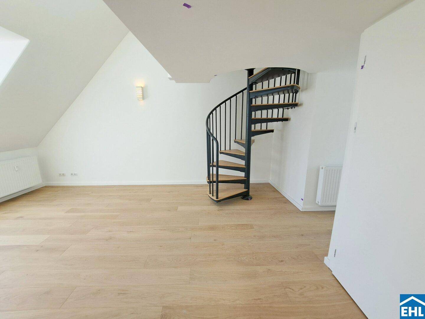 Heller Innenraum mit Holzfußboden, weißen Wänden und einer eleganten Wendeltreppe.