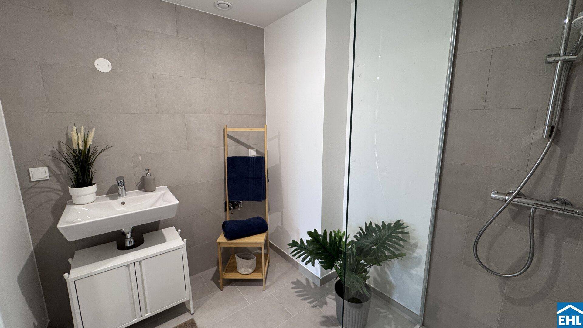 Helles Badezimmer mit moderner Dusche, Einzelwaschbecken und grauen Wandfliesen.
