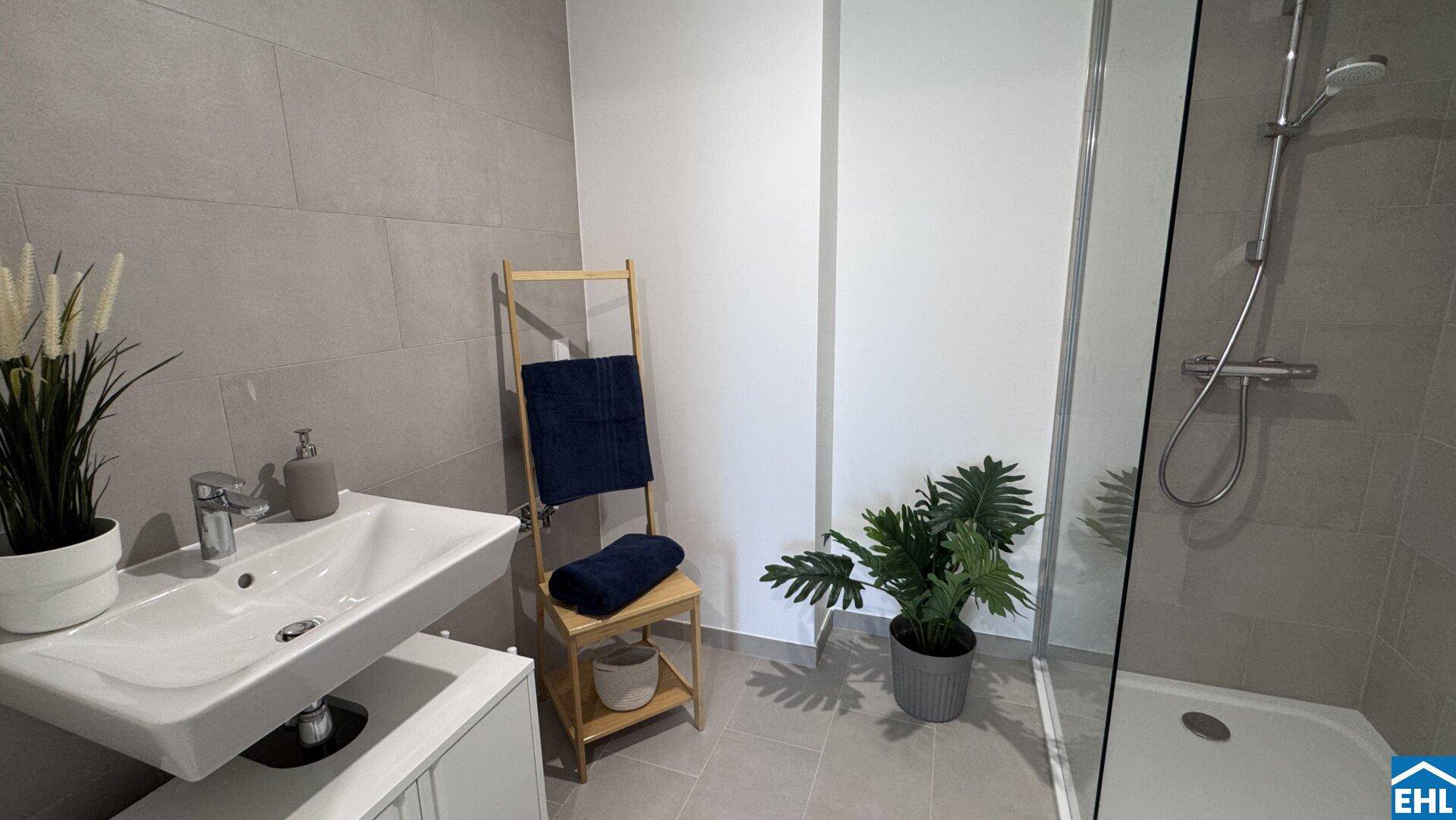 Modernes Badezimmer mit grauen Fliesen, Waschtisch und ebenerdiger Dusche.