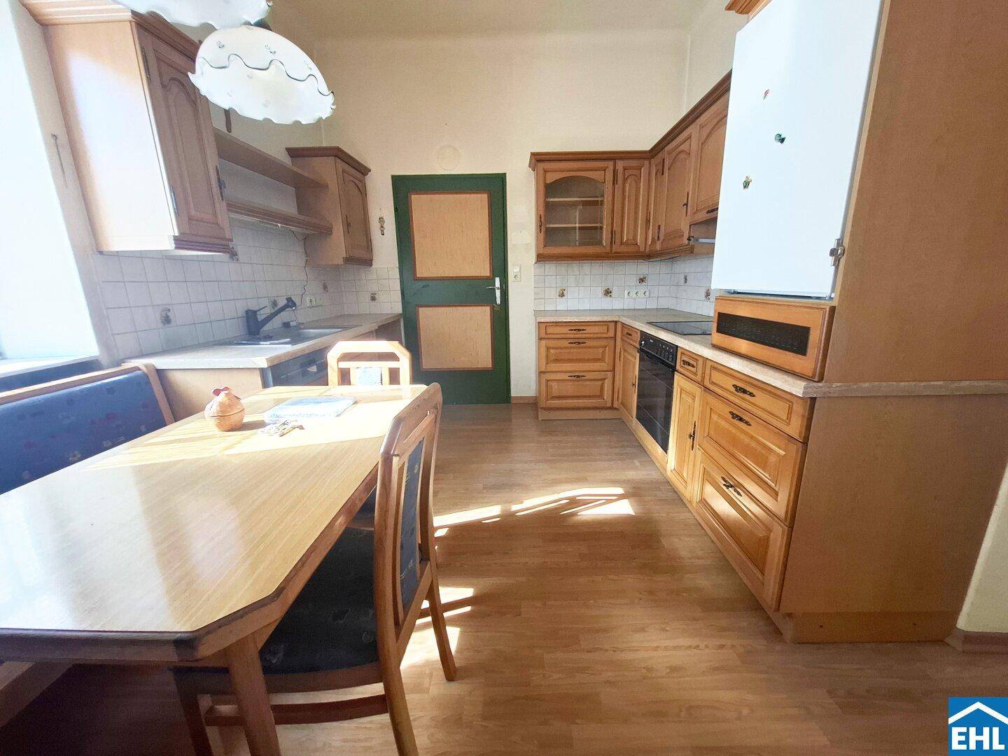 Traditionelle Wohnküche mit Holzschränken, Essbereich und viel Tageslicht.