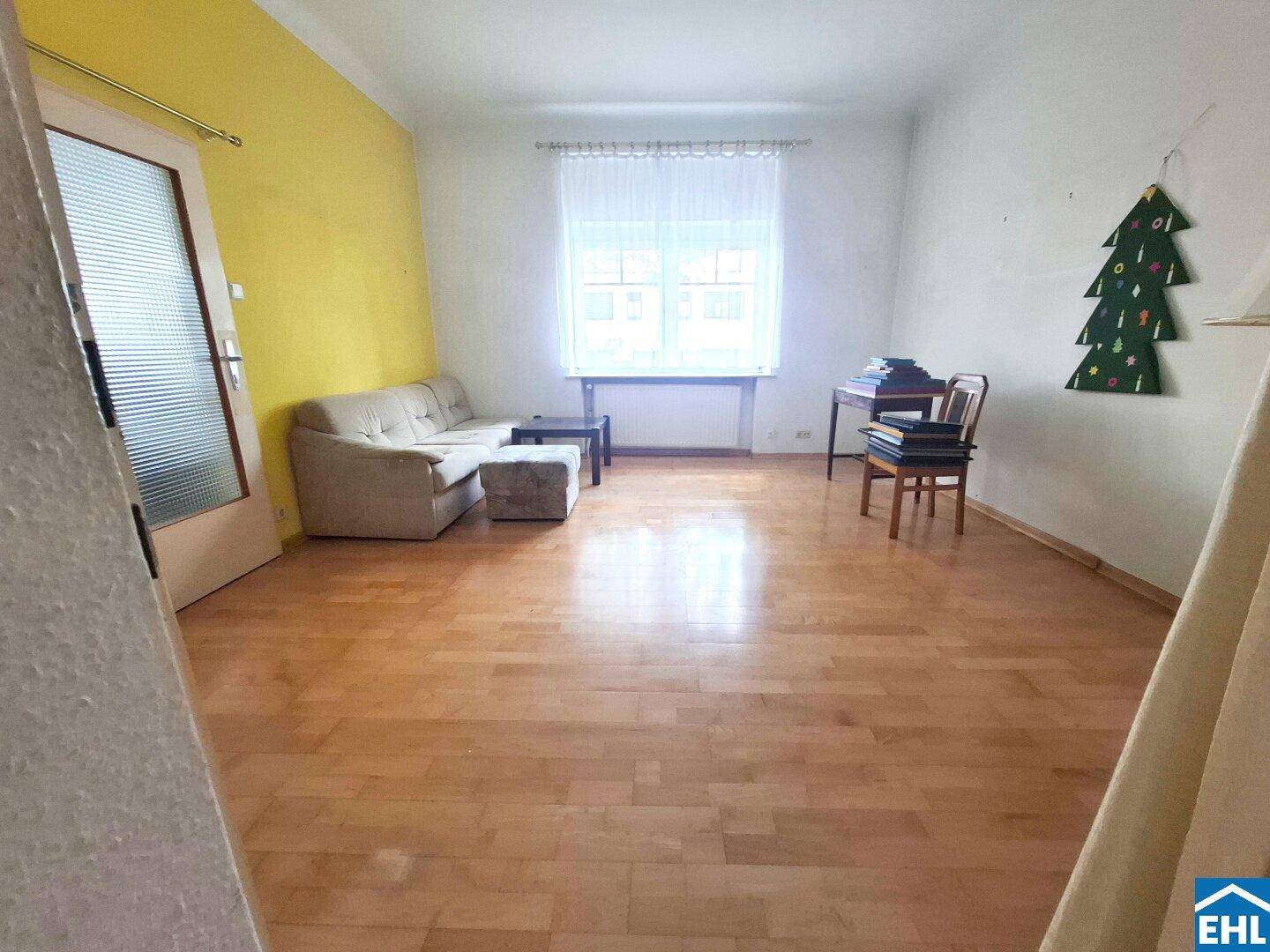 Helles Wohnzimmer mit Holzboden, gelber Akzentwand und großem Fenster.