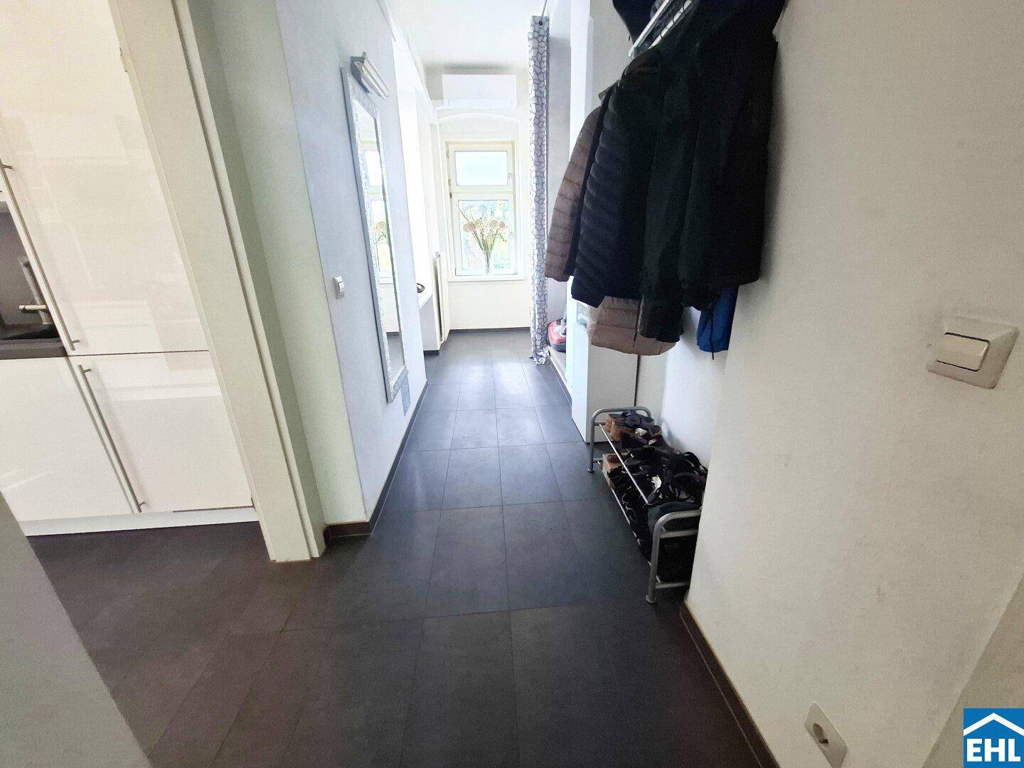 Langer Flur mit dunklem Fliesenboden und Garderobe, der zu weiteren Räumen führt.