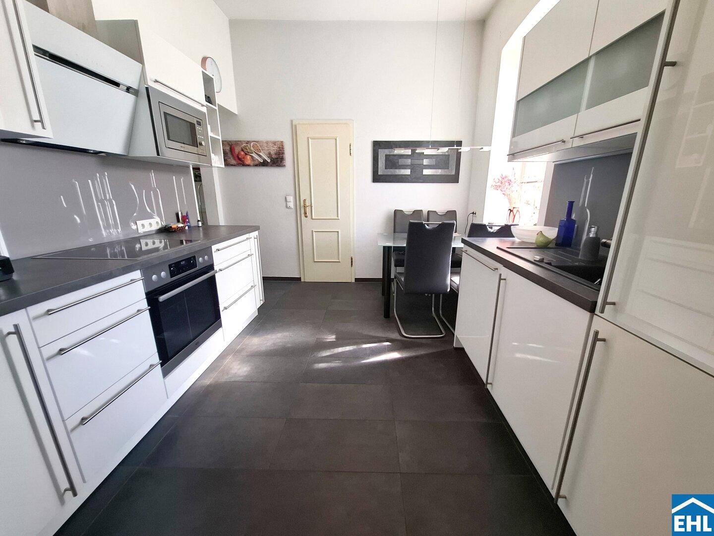Moderne Küche mit weißen Hochglanzfronten, dunkler Arbeitsplatte und integriertem Essbereich.