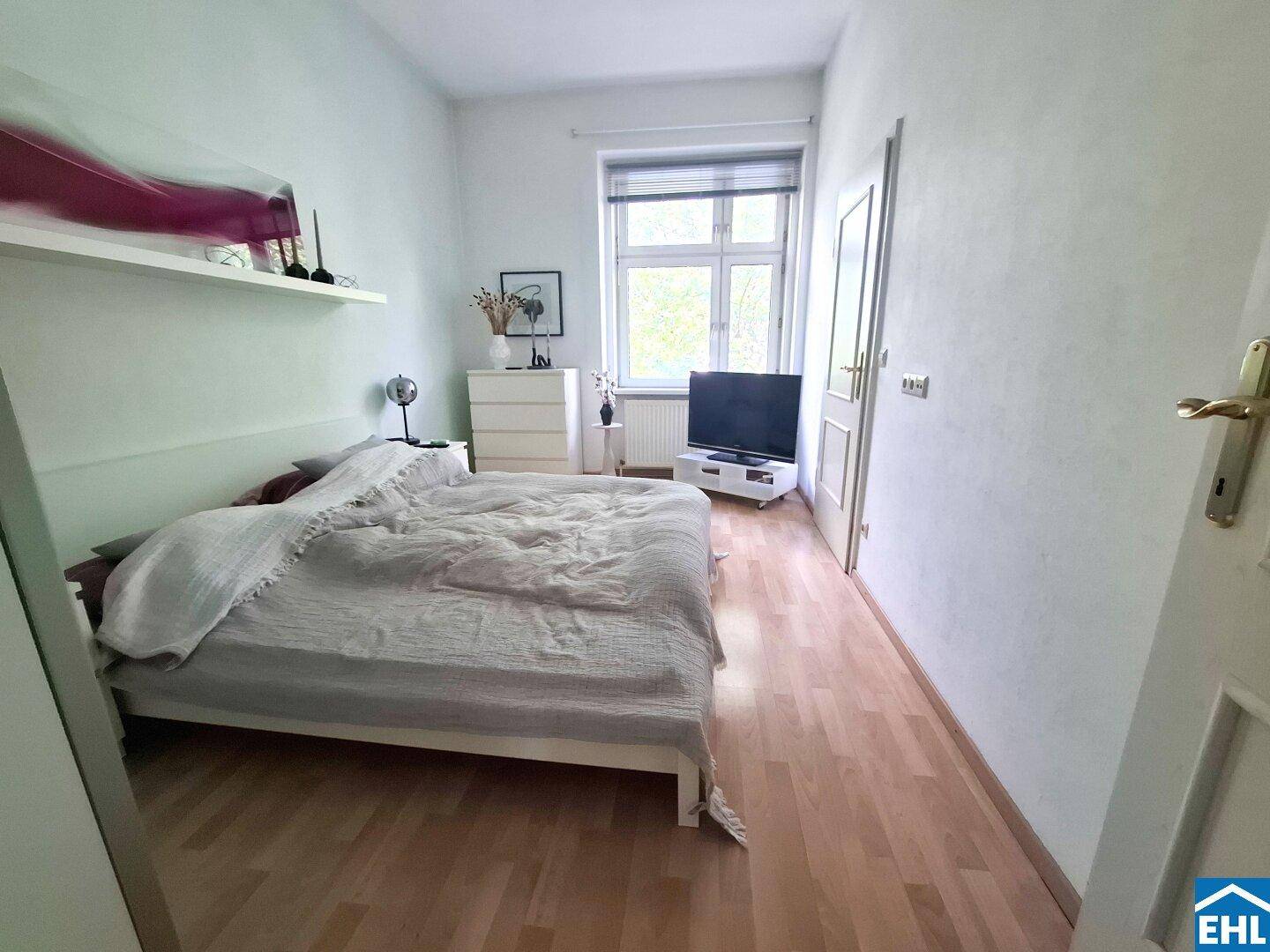 Helles Schlafzimmer mit Holzboden, großem Bett und Fenster mit Blick ins Grüne.