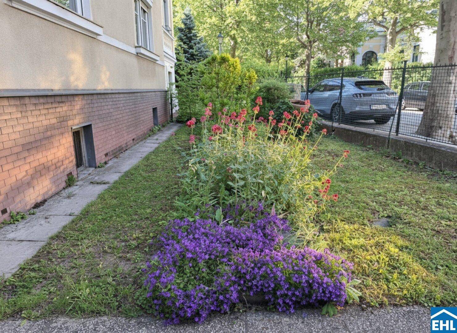 Kleiner Vorgarten mit bunten Blumenbeeten und gepflegter Grünfläche vor dem Gebäude.