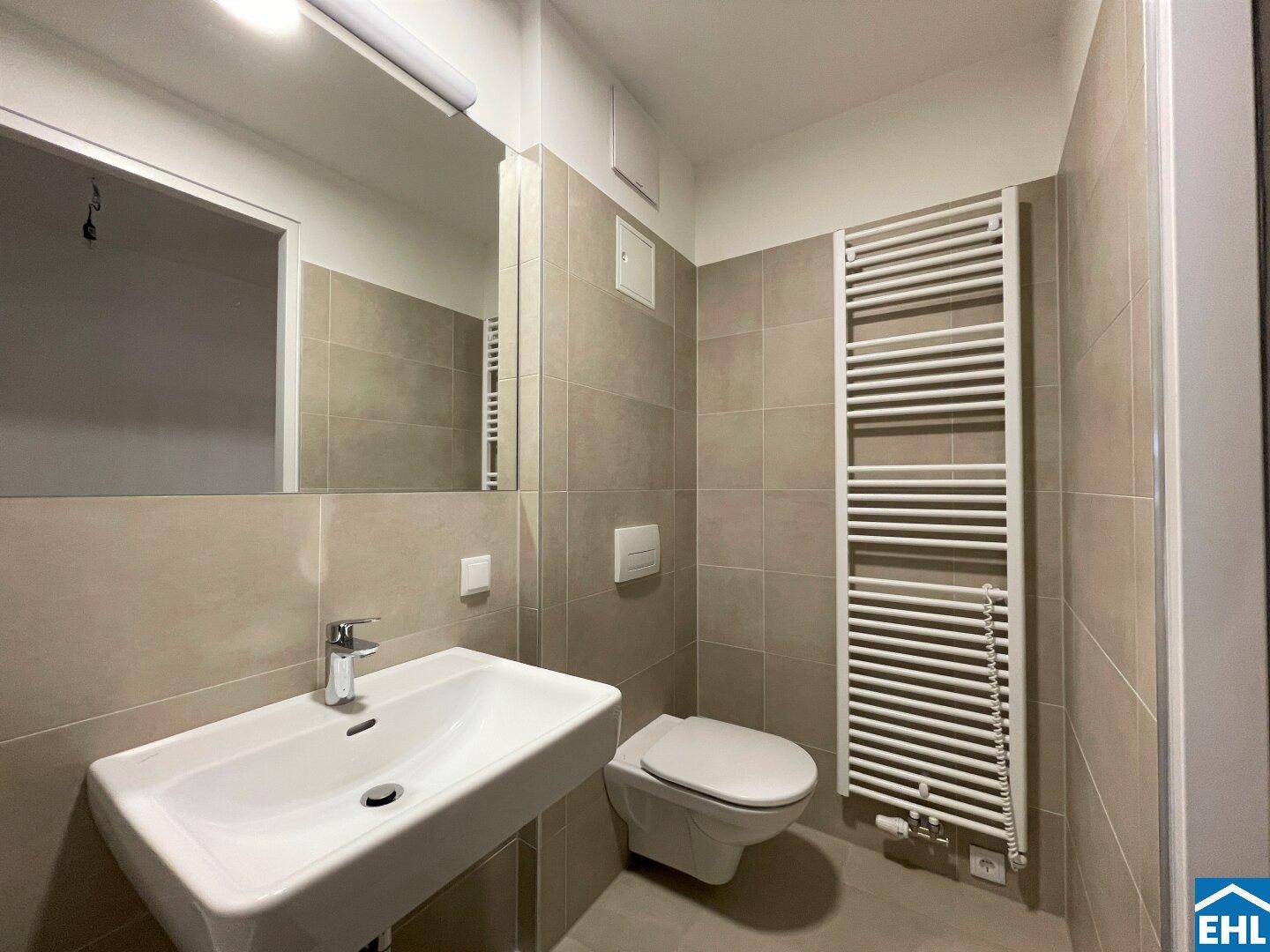 Modernes Badezimmer mit beigefarbenen Fliesen, Waschbecken und beheiztem Handtuchhalter.