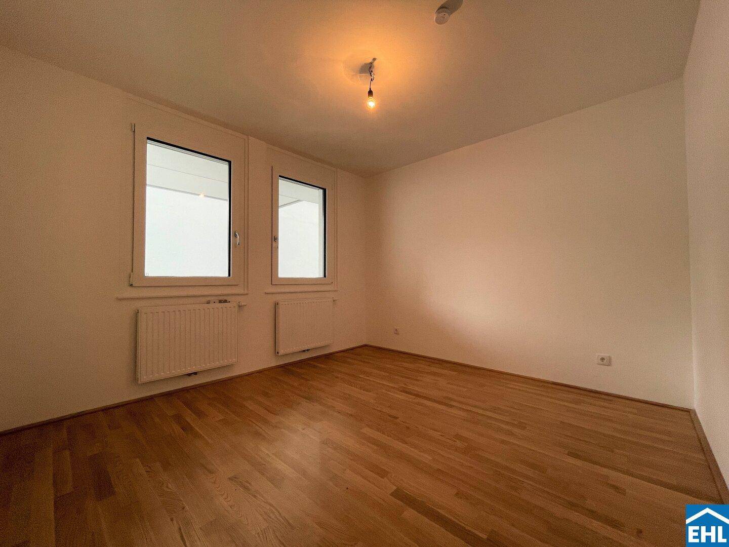 Helles Schlafzimmer mit Parkettboden und zwei Fenstern für viel Tageslicht.