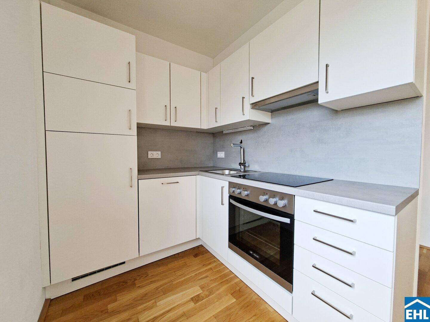 Moderne Einbauküche mit weißen Schränken, integriertem Backofen und Kochfeld.