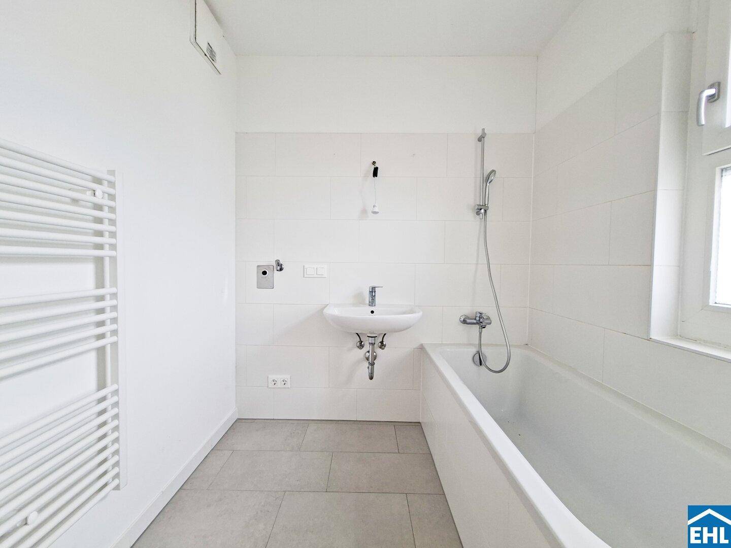 Modernes Badezimmer mit Badewanne, Waschbecken, Handtuchheizkörper und Fenster.