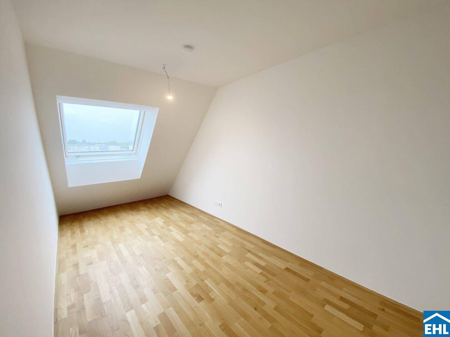 Helles Zimmer im Dachgeschoss mit schrägen Wänden, Holzboden und großem Dachfenster.