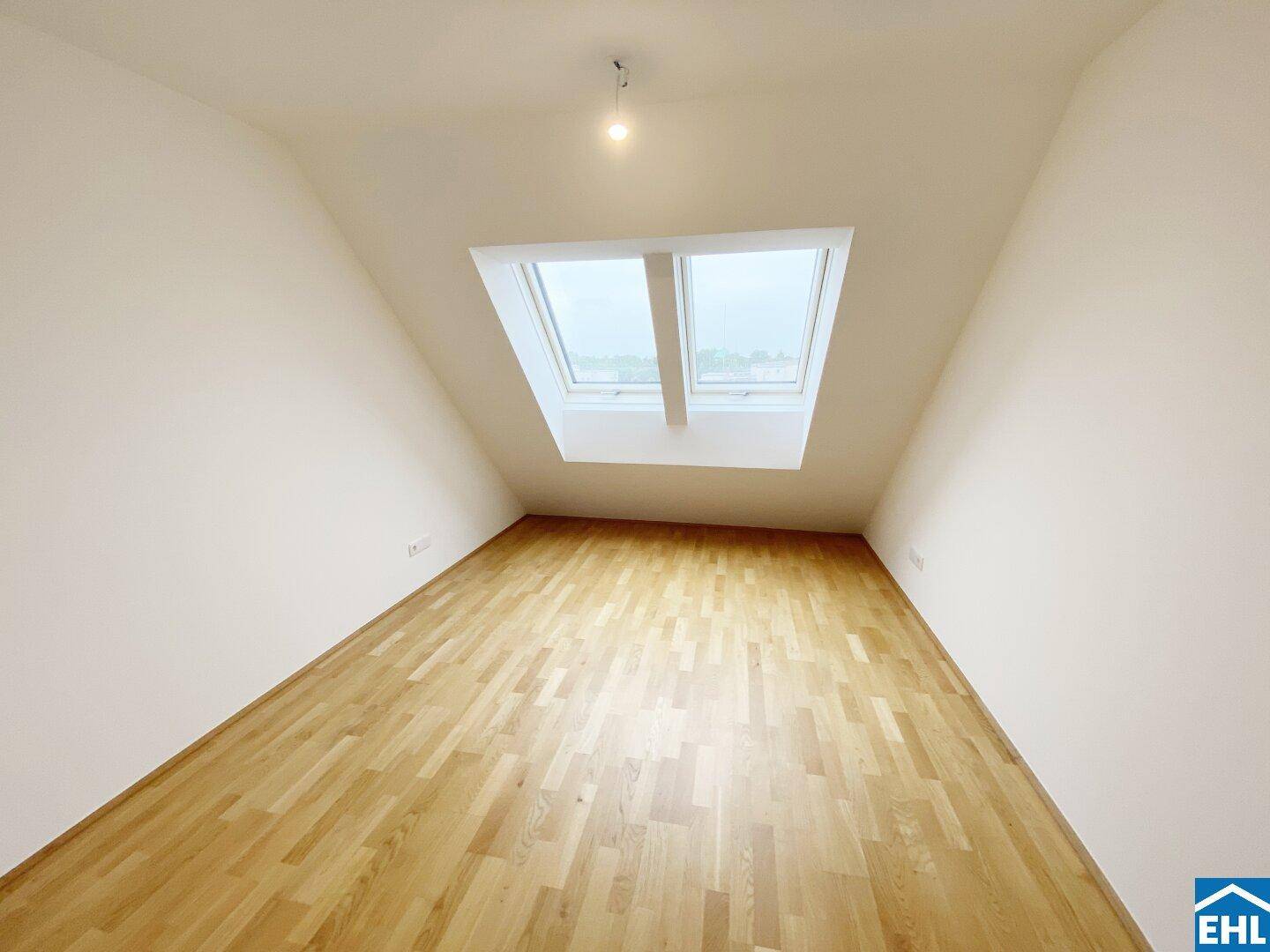 Geräumiges Zimmer im Dachgeschoss mit zwei Dachfenstern und hellem Parkettboden.