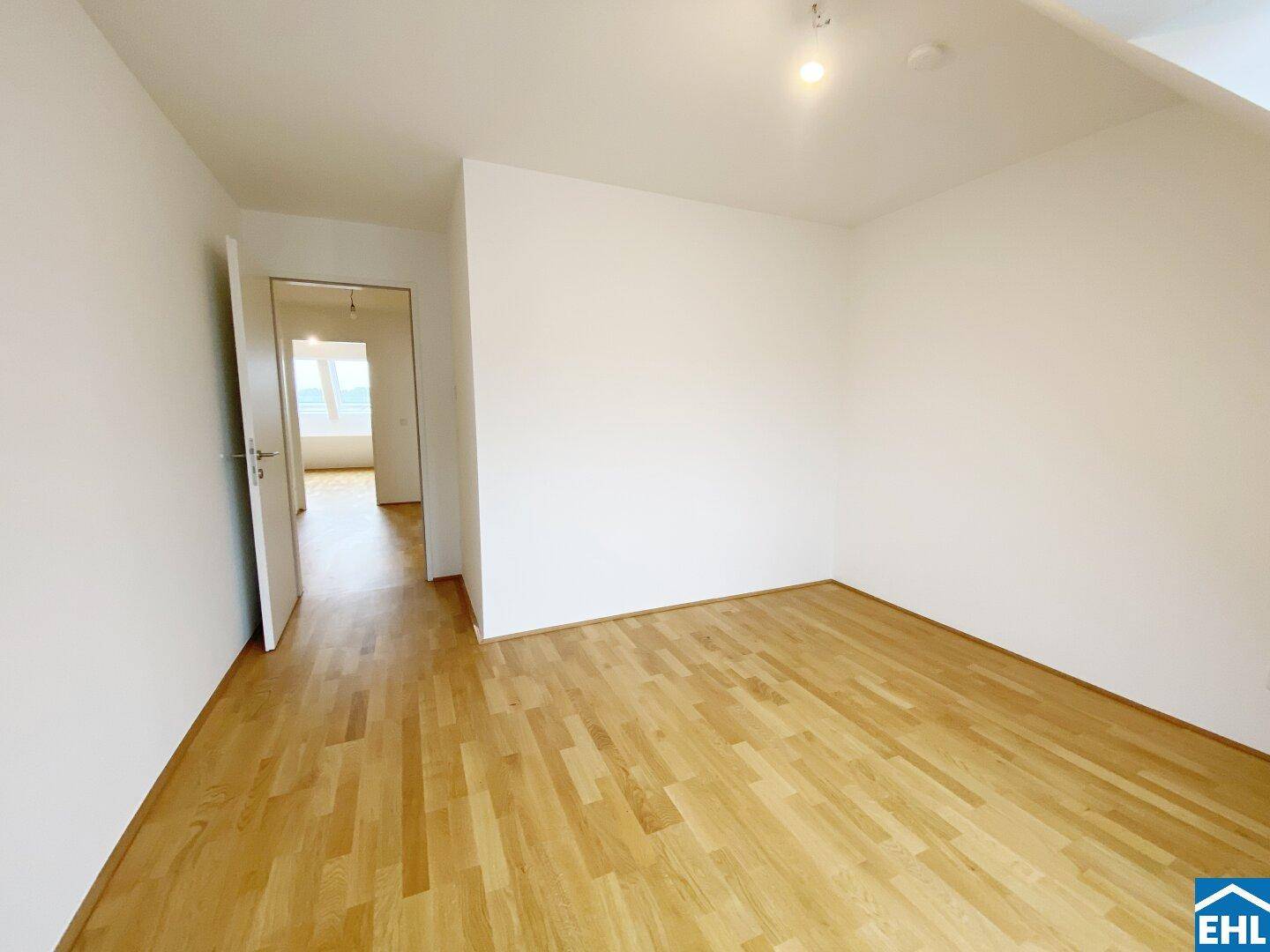 Leeres Zimmer mit hellem Parkettboden und weiß gestrichenen Wänden, Blick in den Flur.