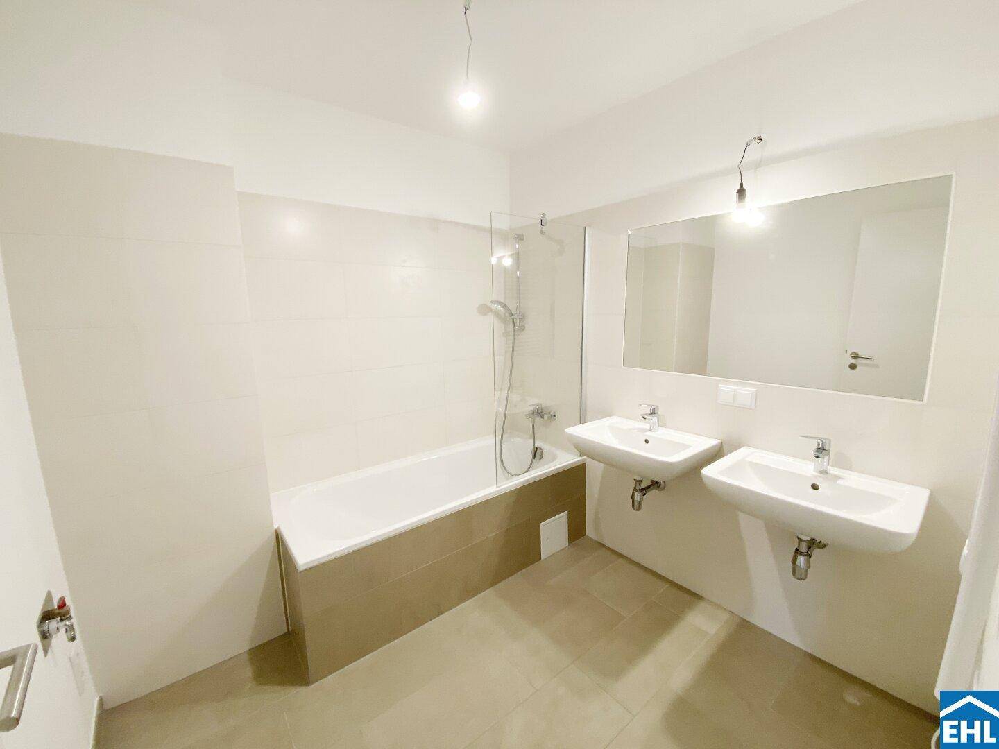 Modernes Badezimmer mit Doppelwaschbecken, Badewanne und hellen Fliesen.