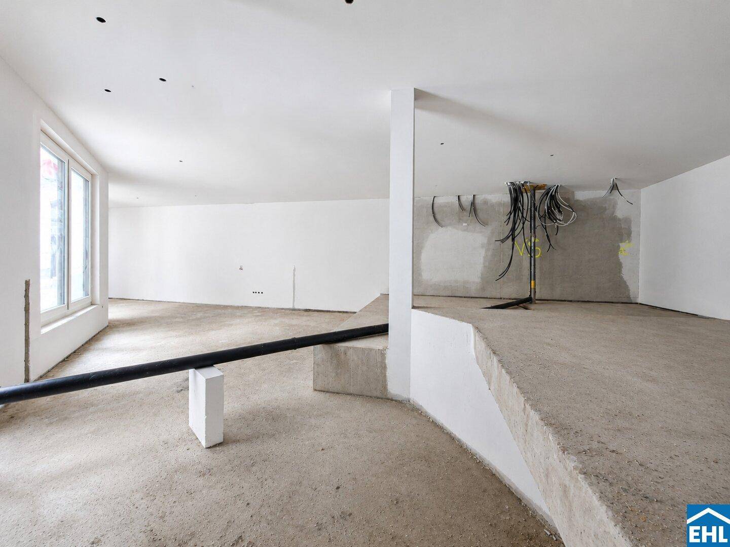 Weitläufiger, unfertiger Innenraum mit Betonboden, weißen Wänden und sichtbaren Kabeln für zukünftige Installationen.