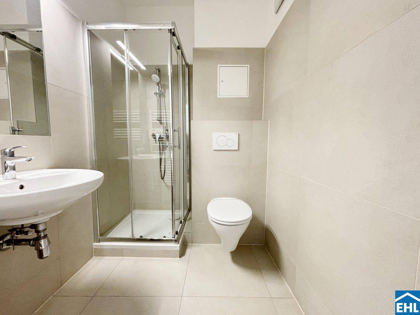 Modernes Badezimmer mit beigefarbenen Fliesen, Dusche und wandhängendem WC.