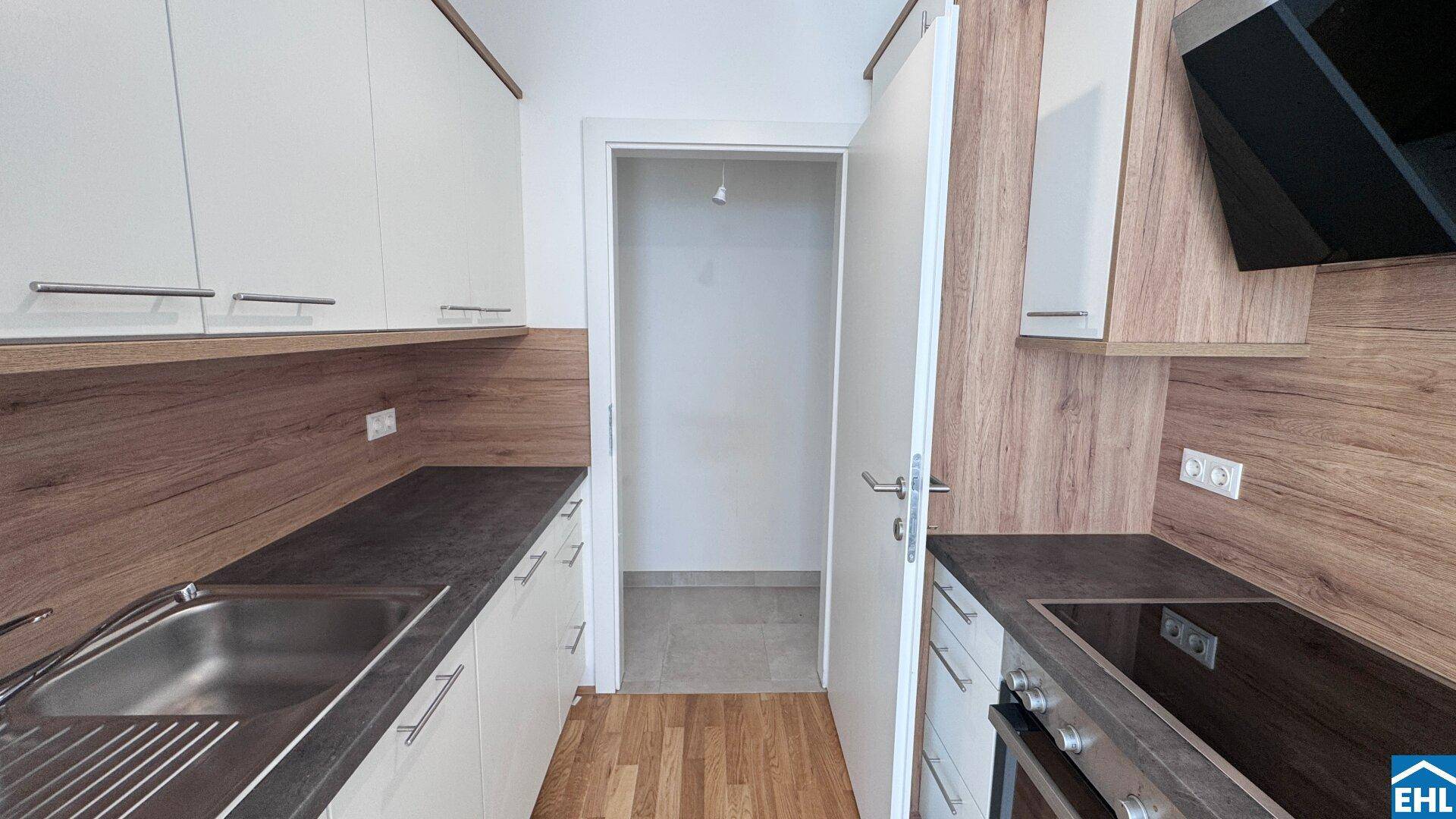 Moderne Einbauküche mit weißen Schränken, Holzdekor und dunkler Arbeitsplatte, bietet Zugang zu einem weiteren Raum.