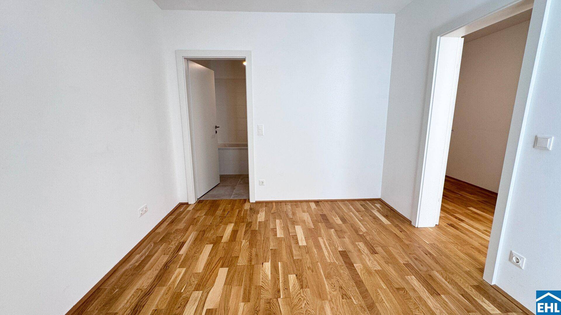 Leeres Zimmer mit Holzboden und zwei Türen, bietet Flexibilität für verschiedene Nutzungen.