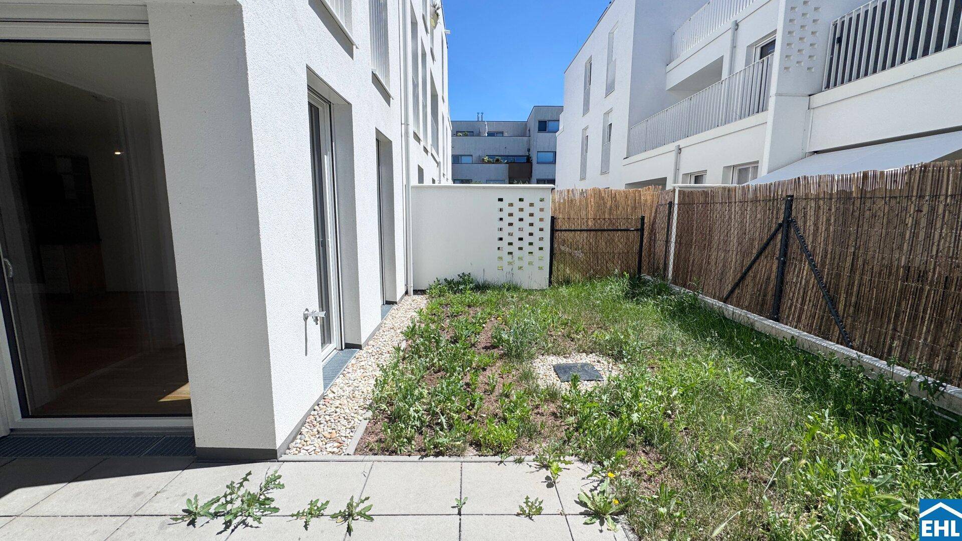 Kleiner privater Gartenbereich mit Terrasse und Blick auf die moderne Wohnanlage.