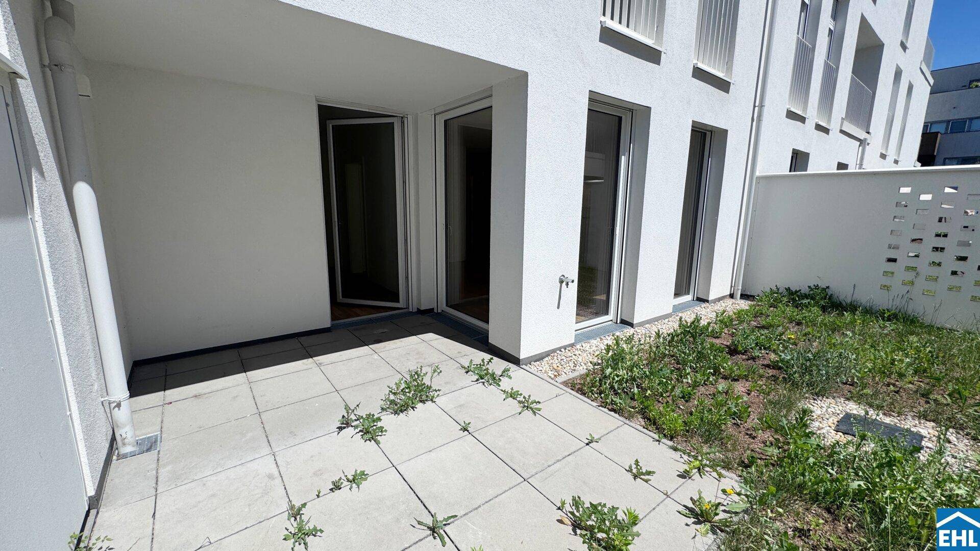 Sonniger Terrassenbereich mit angrenzendem Garten, umgeben von moderner Architektur.