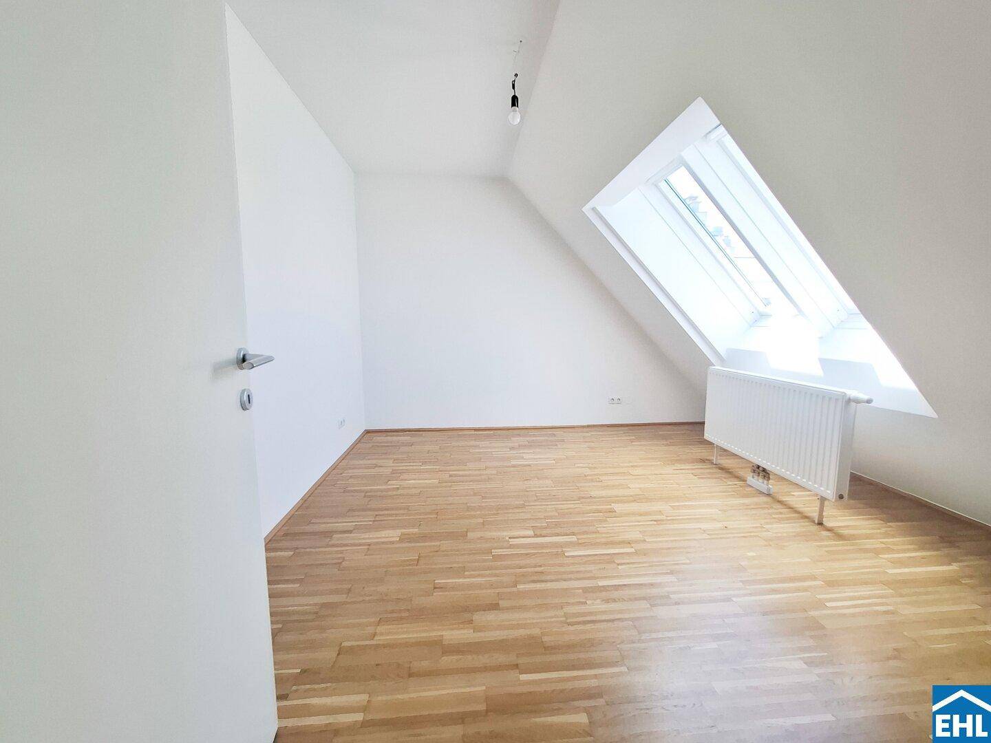 Helles Dachzimmer mit Parkettboden und großem Dachfenster, das viel Licht spendet.