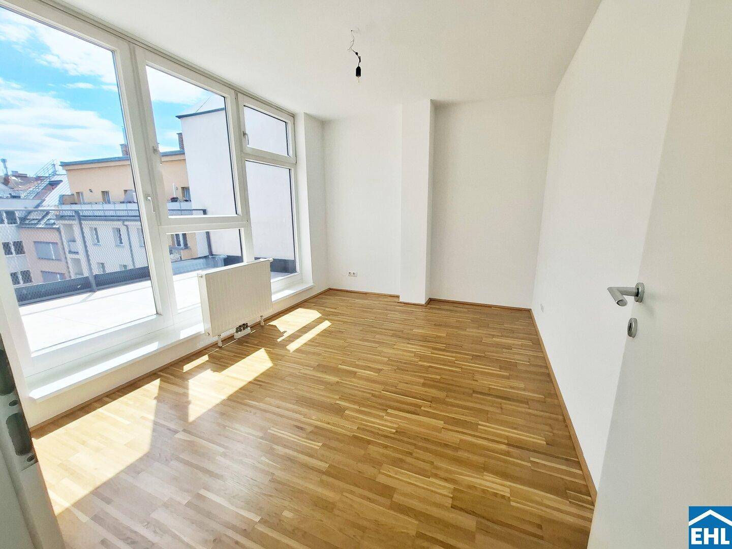 Lichtdurchflutetes Zimmer mit Parkettboden und großen Fenstern, die einen weiten Blick bieten.