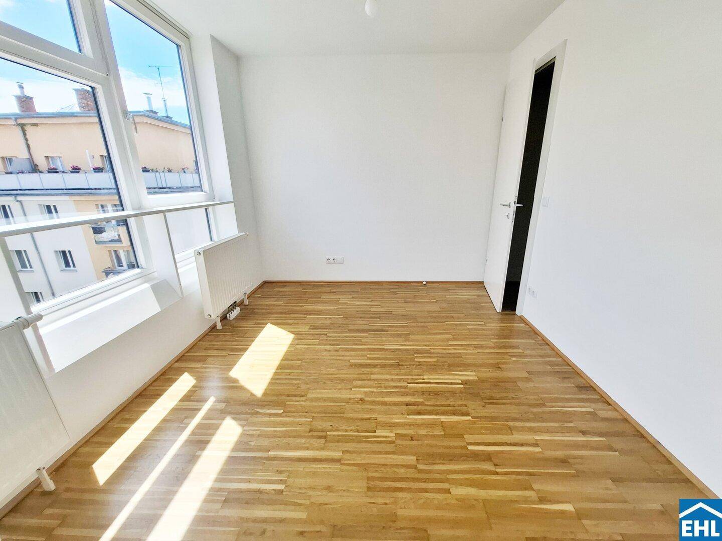 Geräumiges Zimmer mit Parkettboden und großen Fenstern, ideal als Schlaf- oder Arbeitszimmer.