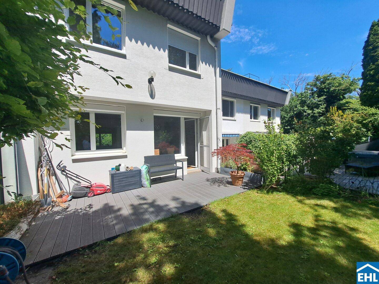 Garten mit Holzterrasse, Rasenfläche und üppiger Bepflanzung, ideal zum Entspannen.