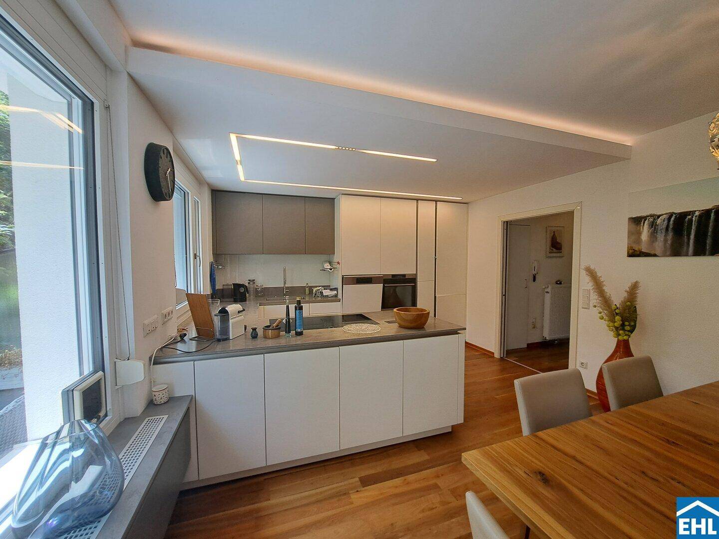 Moderne offene Küche mit Kochinsel, Holzboden und integrierter Deckenbeleuchtung.