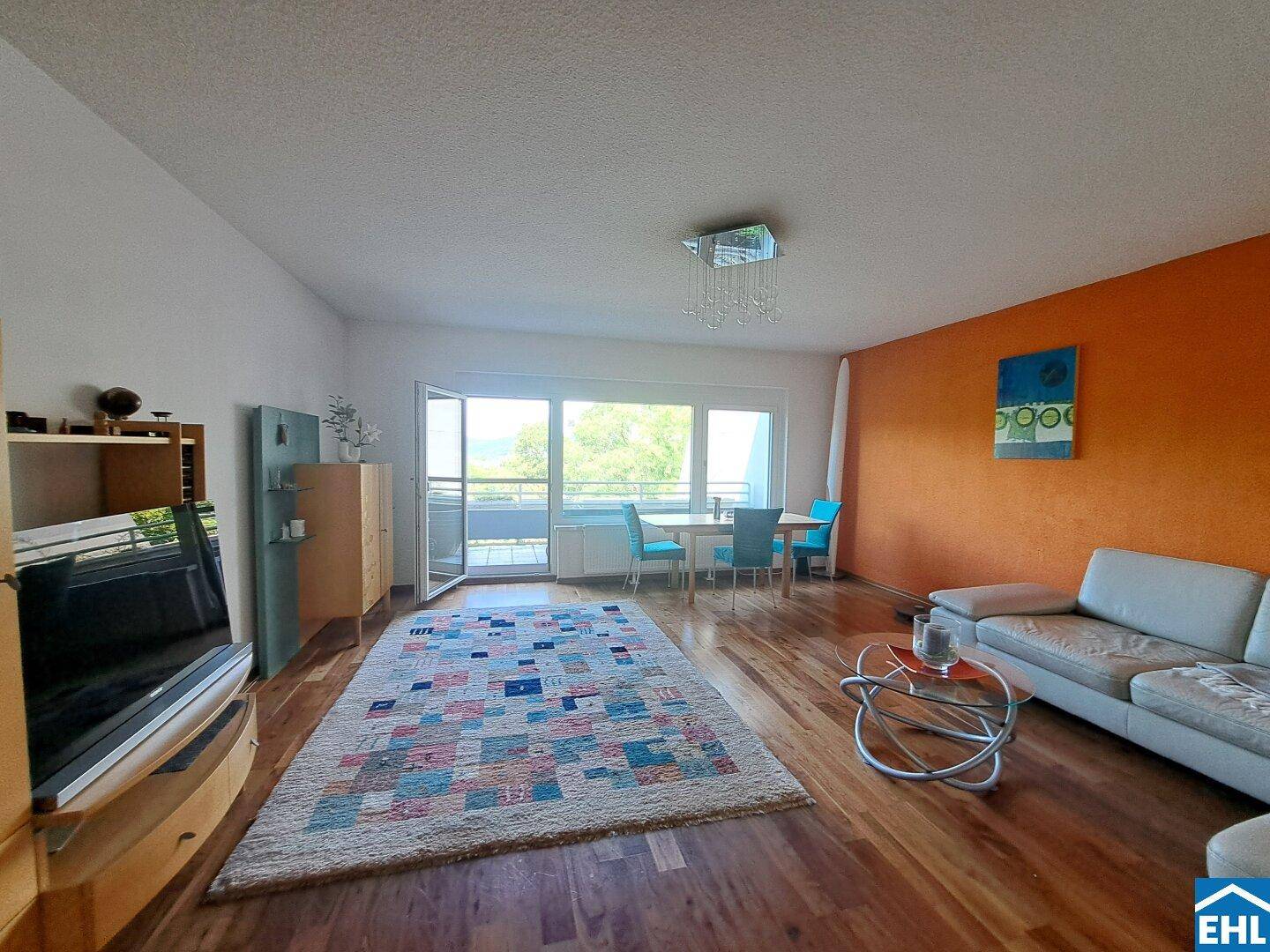 Geräumiges Wohnzimmer mit Holzboden, farbiger Akzentwand und Zugang zum Balkon.