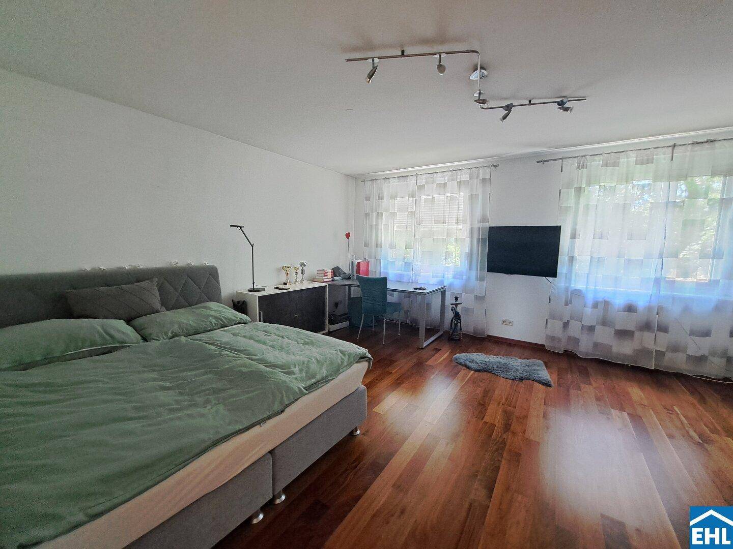 Helles Schlafzimmer mit Holzboden, großem Bett und einem Arbeitsbereich am Fenster.