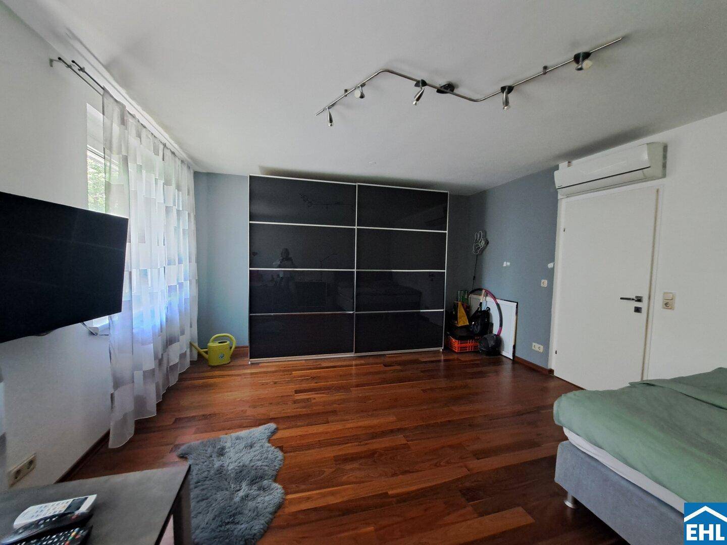 Schlafzimmer mit Holzboden, großem schwarzen Schiebetürenschrank und Klimaanlage.