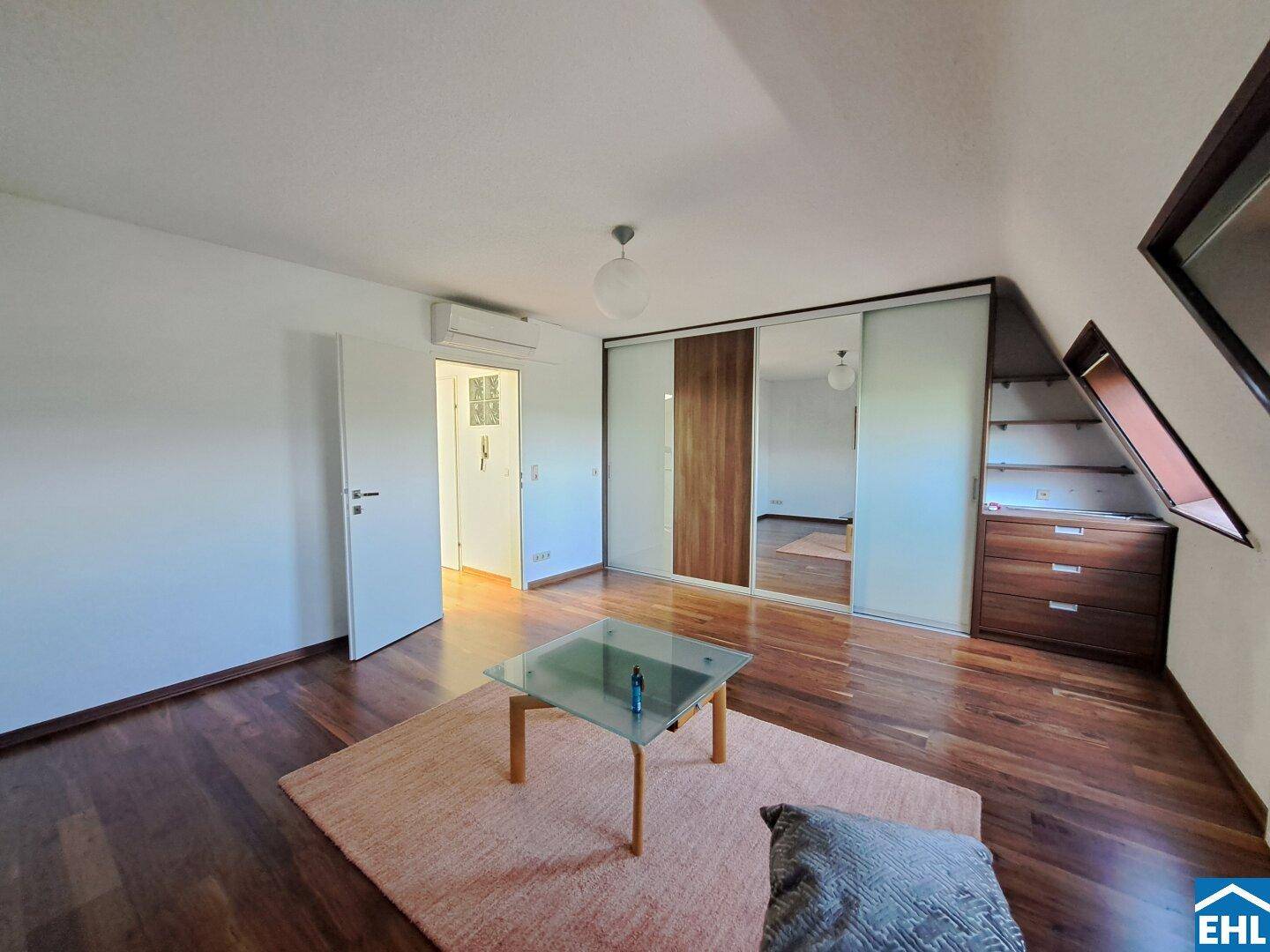Dachzimmer mit Holzboden, Einbauschränken und Klimaanlage unter der Dachschräge.