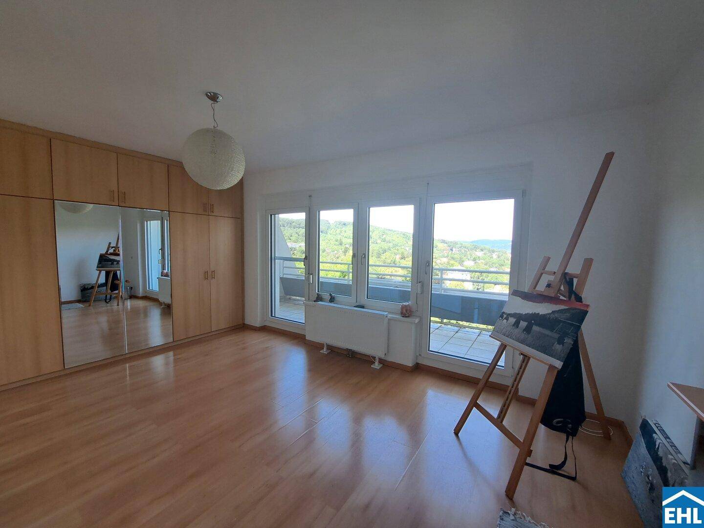 Helles Zimmer mit Laminatboden, Einbauschränken und Zugang zu einem Balkon.
