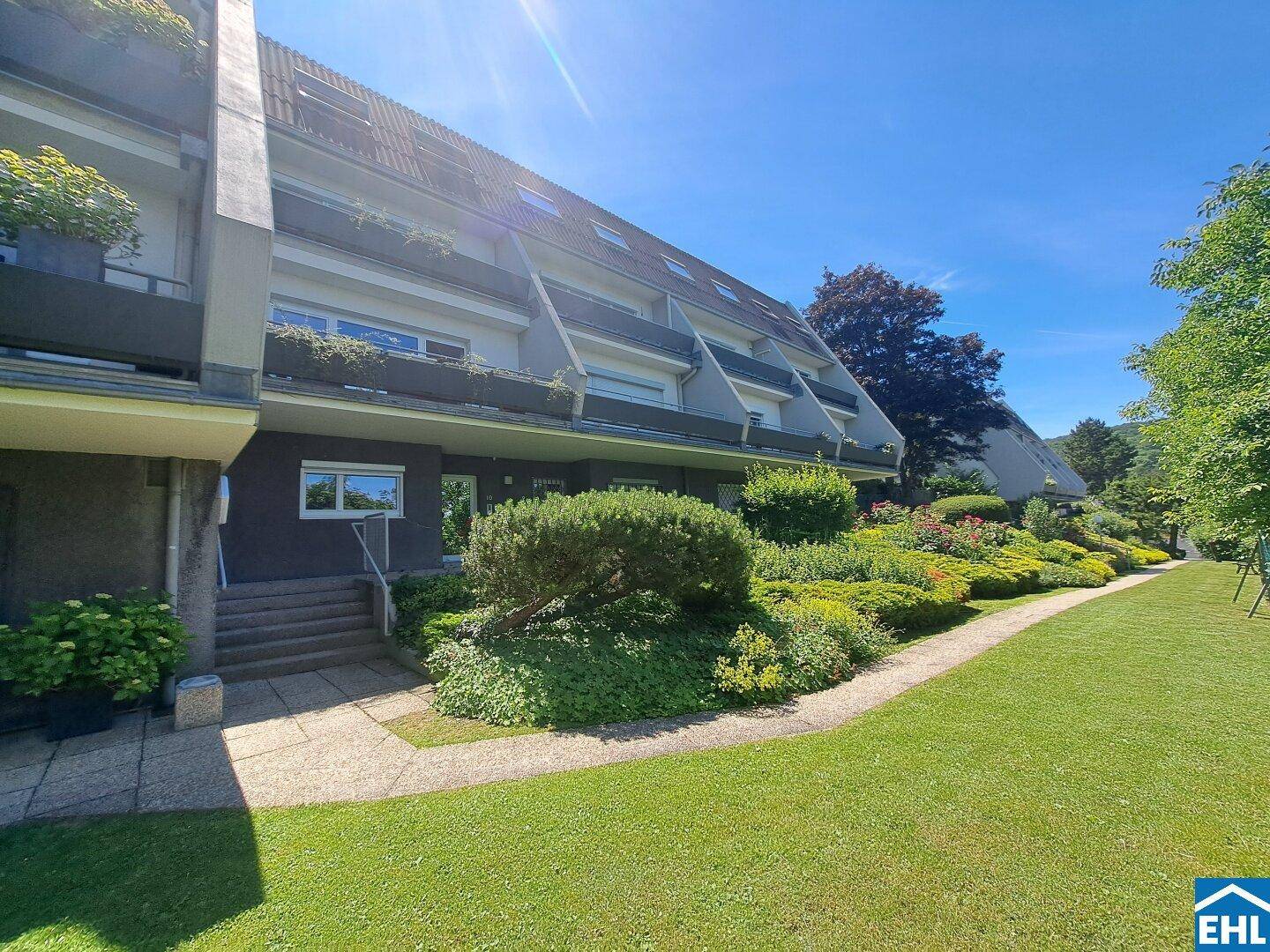 Mehrfamilienhaus mit gepflegter Gartenanlage und sonniger Fassade an einem hellen Tag.