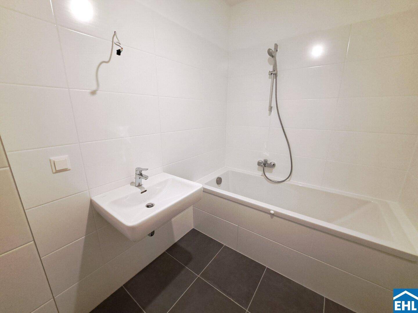 Modernes Badezimmer mit weißen Wandfliesen, Badewanne mit Duschfunktion und einem einzelnen Waschbecken.