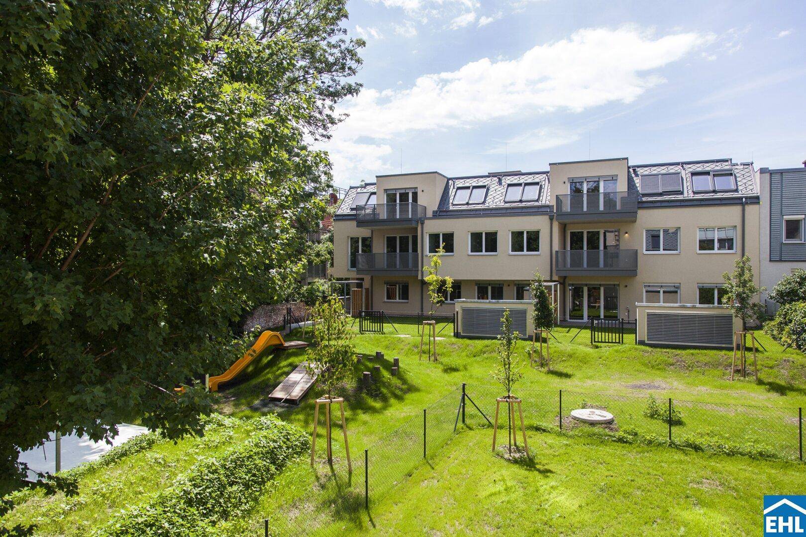 Moderne Wohnanlage mit gepflegter Grünfläche und Spielplatz für Kinder, umgeben von Bäumen.