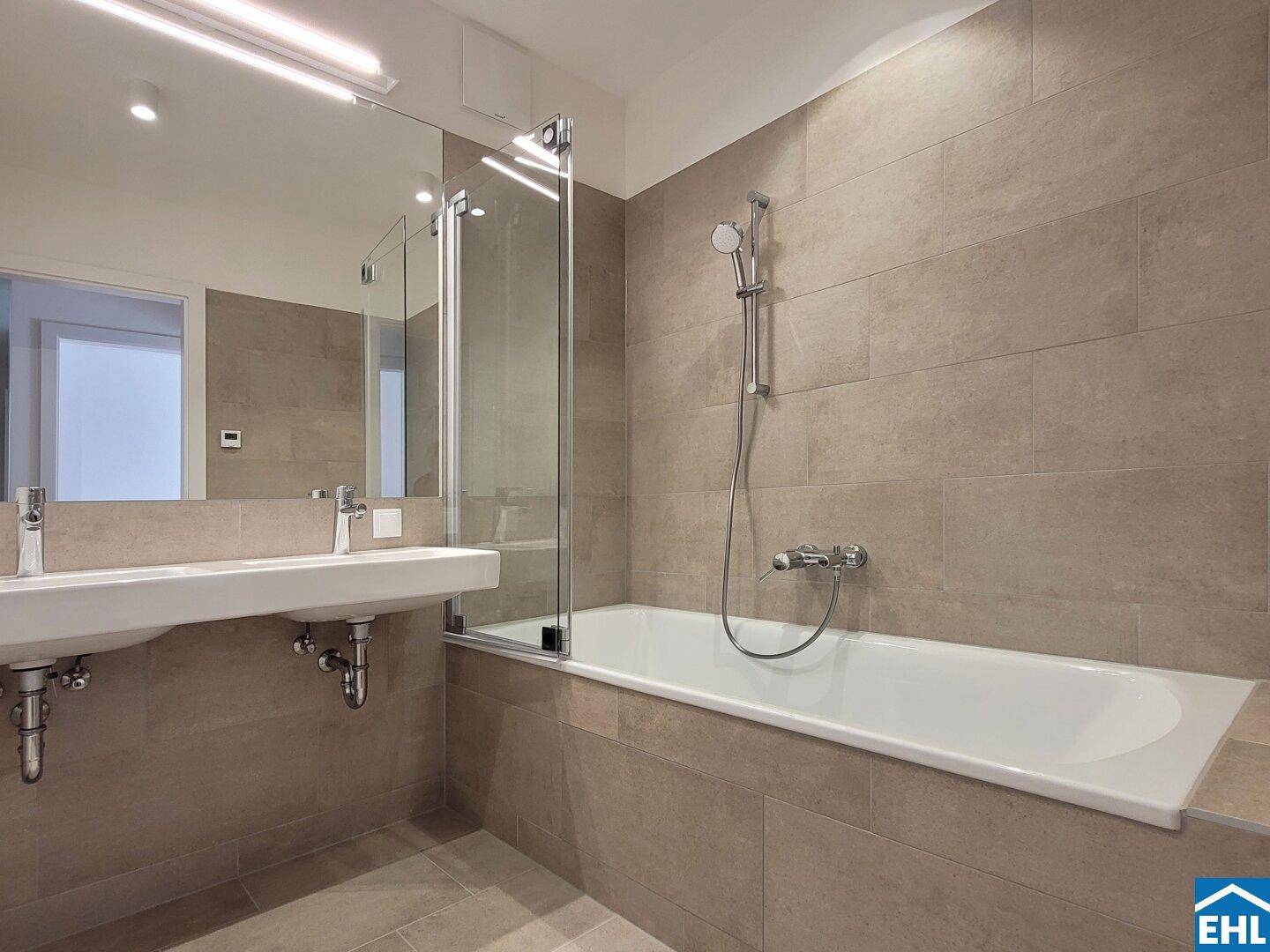 Modernes Badezimmer mit doppelten Waschbecken, Badewanne und beigefarbenen Fliesen.