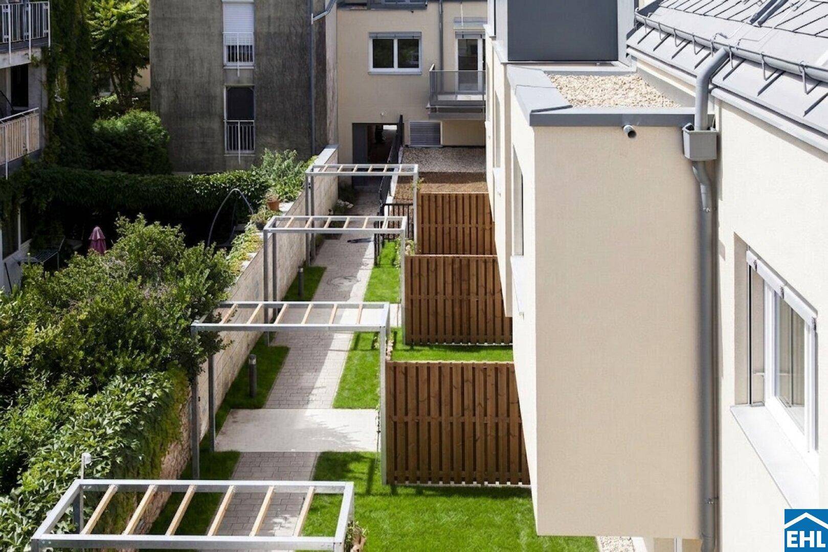 Seitlicher Blick auf die Wohnanlage mit privaten Gartenbereichen und gepflasterten Wegen.
