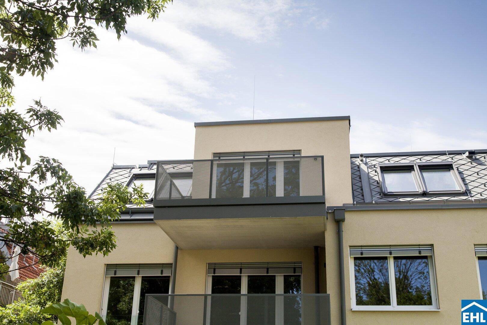 Moderner Balkon mit Glasgeländer und Blick auf die Umgebung, unter einem Mansarddach.