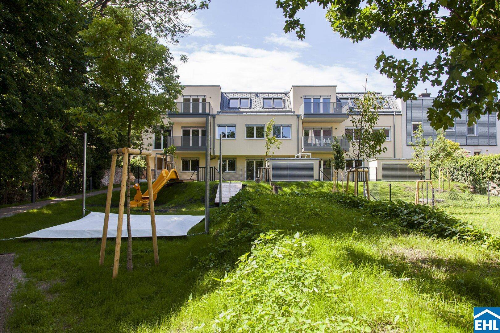 Rückansicht eines modernen Wohnkomplexes mit großzügiger Grünfläche und Kinderspielplatz.