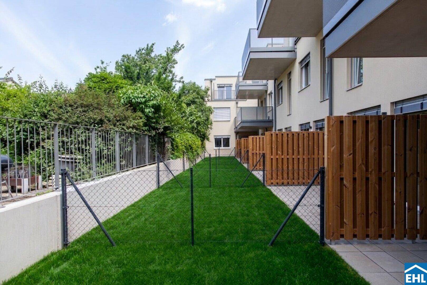 Schmaler, gepflegter Gartenstreifen mit Kunstrasen und Holzzäunen zwischen den Gebäuden.