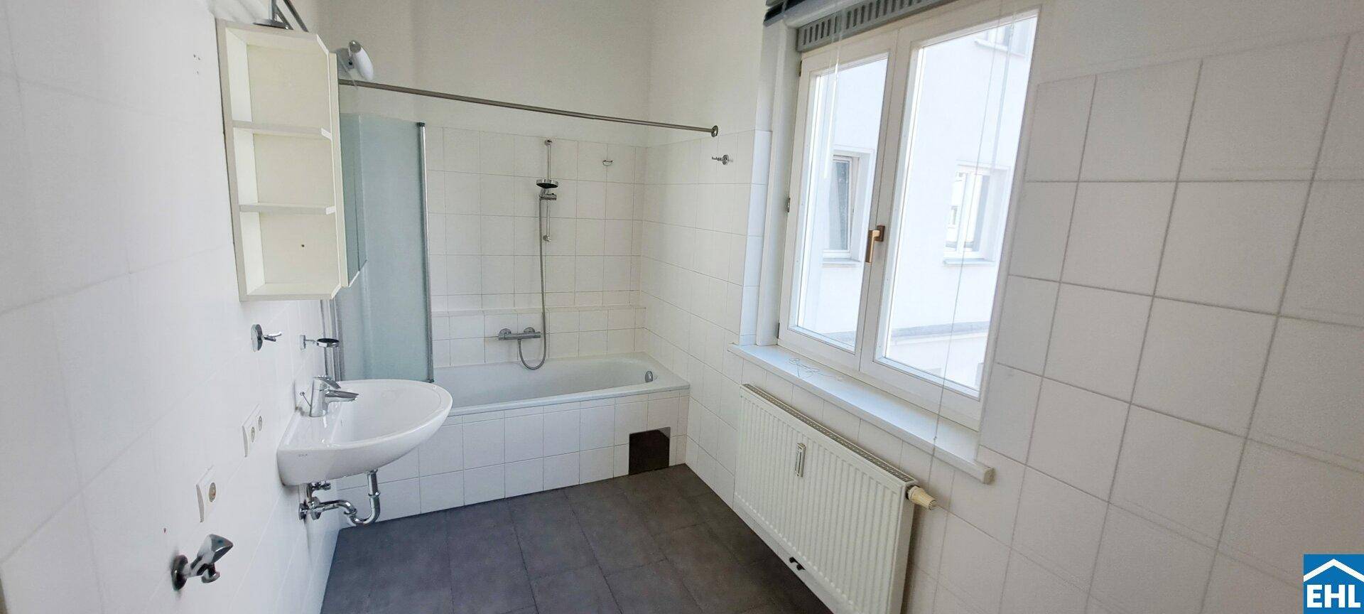Helles Badezimmer mit Badewanne, Duschvorrichtung, Waschbecken und Fenster für natürliche Belüftung.