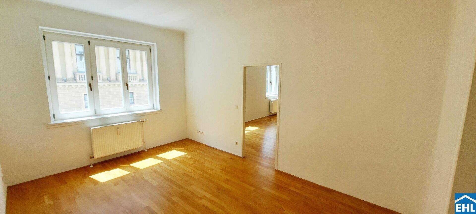 Heller Raum mit Parkettboden und großem Fenster, das den Raum mit Sonnenlicht durchflutet.