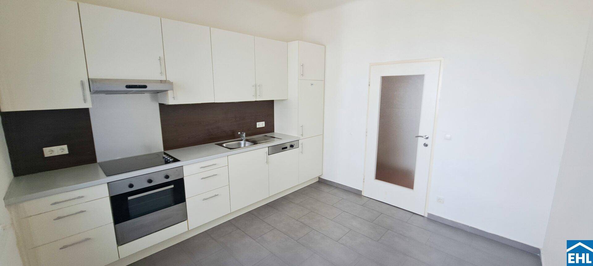 Moderne Einbauküche mit weißen Schränken, integrierten Geräten und grauem Fliesenboden.