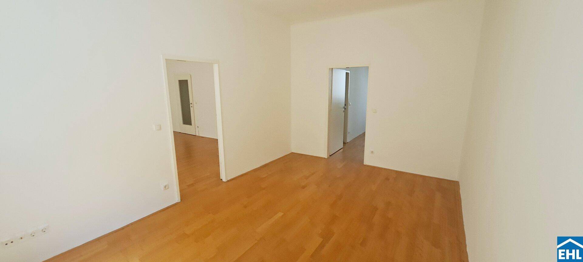 Geräumiges Zimmer mit hellem Parkettboden und Zugang zu weiteren Räumen.