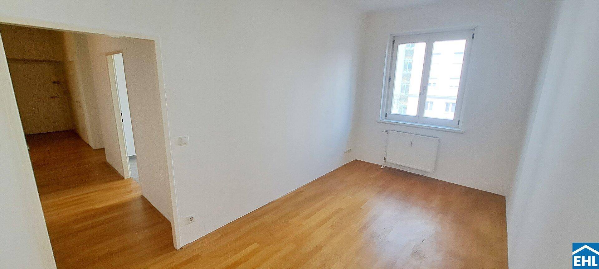 Gemütliches Schlafzimmer mit Parkettboden und einem Fenster, das viel Tageslicht hereinlässt.