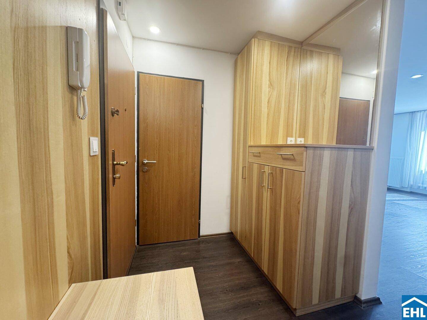 Heller Flur mit Holzmöbeln, Spiegelfläche und Zugang zu weiteren Räumen.