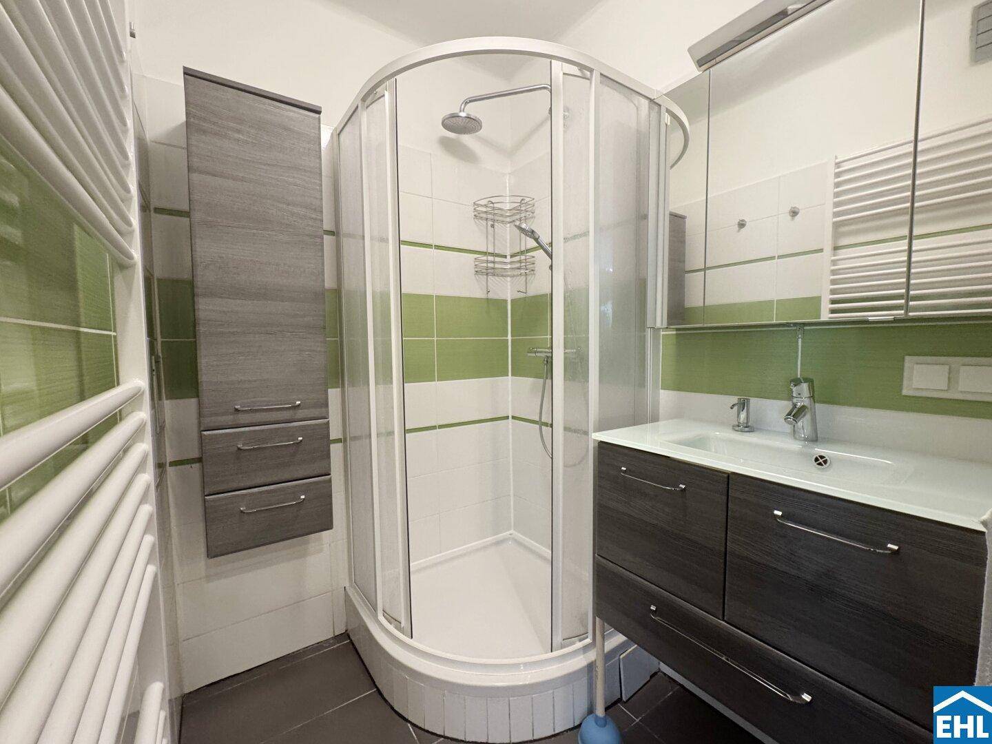 Modernes Badezimmer mit Duschkabine, Waschbecken und grün-weißen Fliesen.