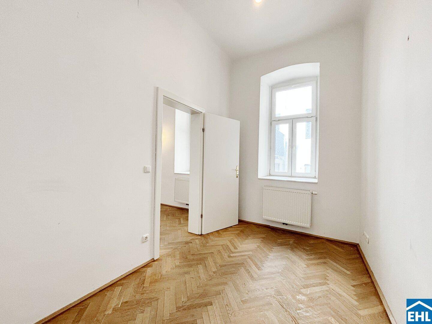 Helles Schlafzimmer mit Parkettboden und einem Fenster, das viel Tageslicht hereinlässt.