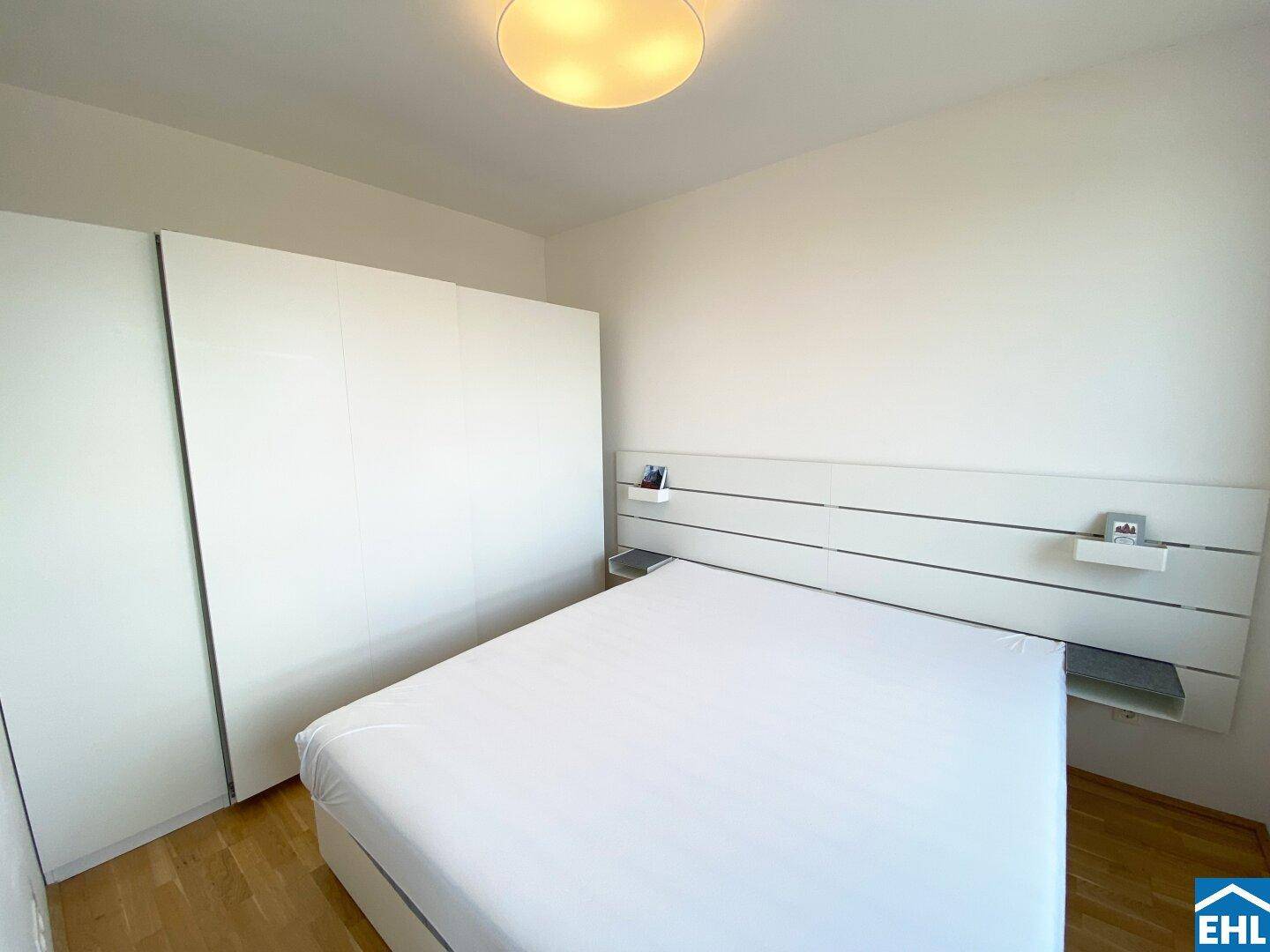Schlafzimmer mit großem Bett, integriertem Kopfteil und geräumigem, weißem Einbauschrank.